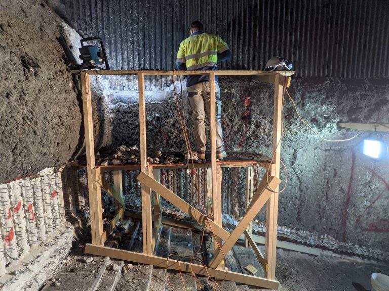 A worker on a timber scaffold jackhammering some old refractories away